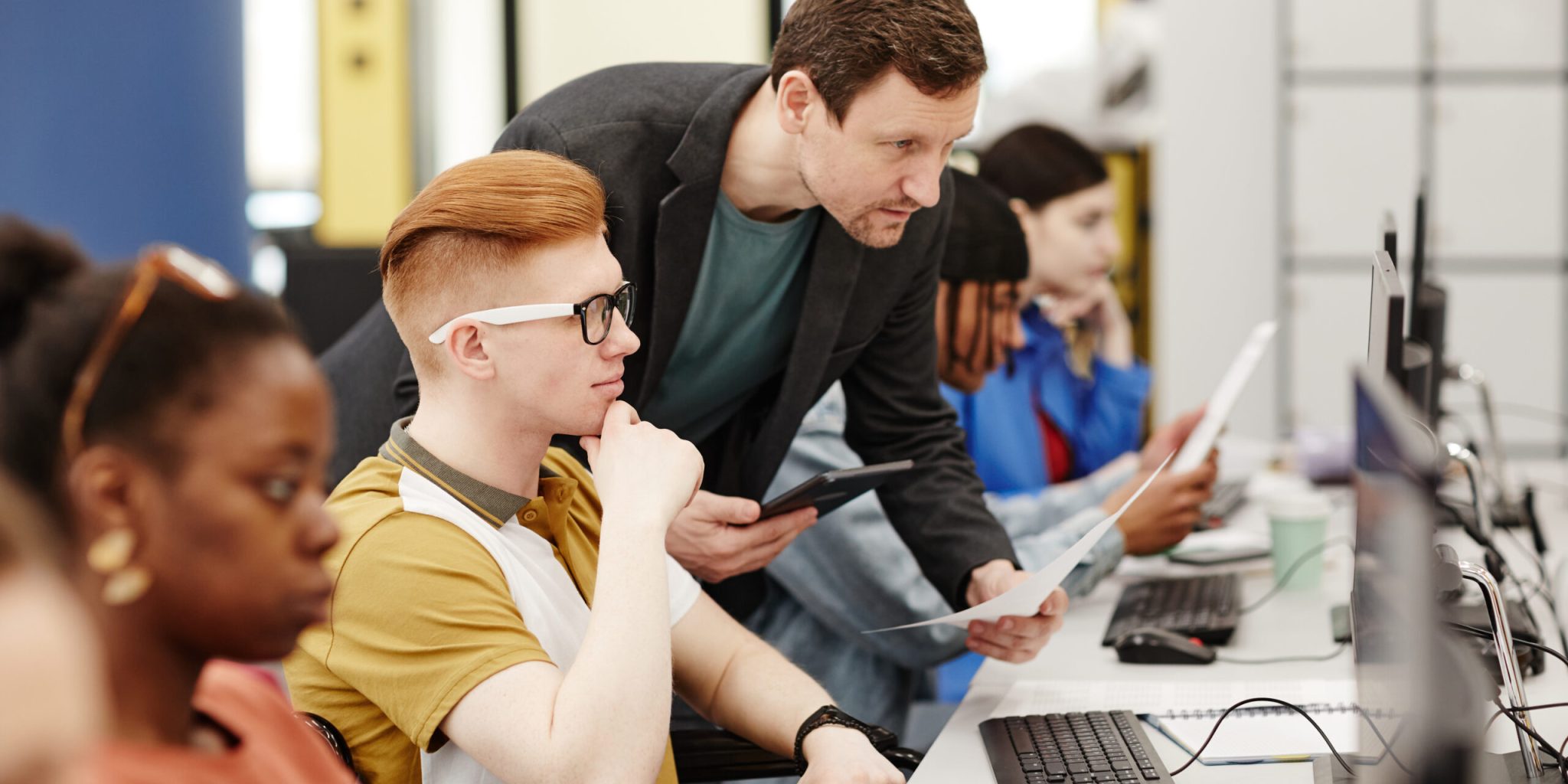 Vibrant side view portrait of male teacher helping student using computer in college classroom, copy space